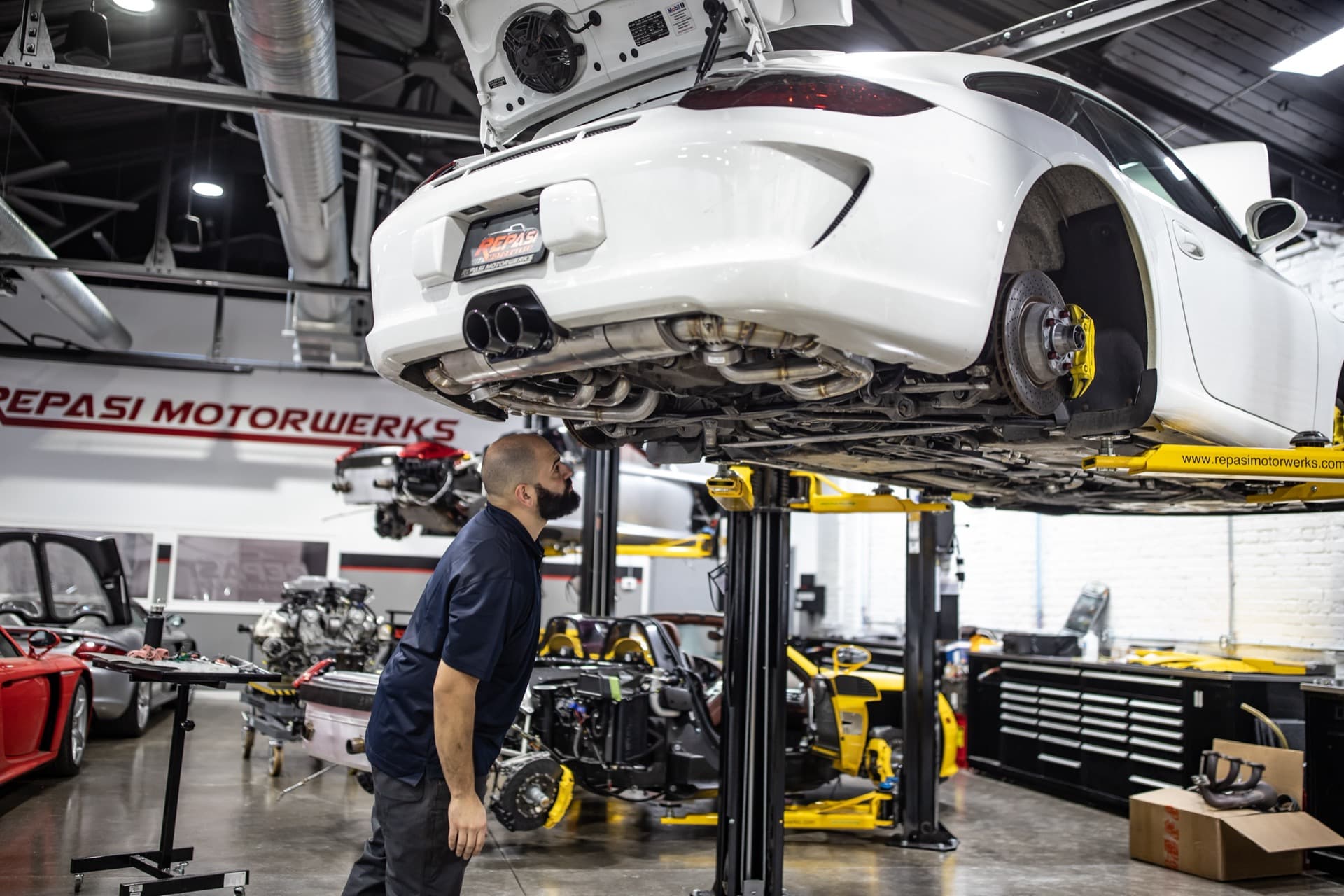 Technician inspecting the underside of a white Porsche 991 GT3 on the lift during a pre-purchase inspection